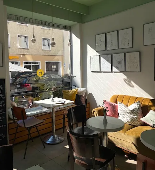 Gemütlicher Gastraum des Cafés Haltestulle in Bielefeld mit Sofa, Bistrotischen und Kunst an der Wand